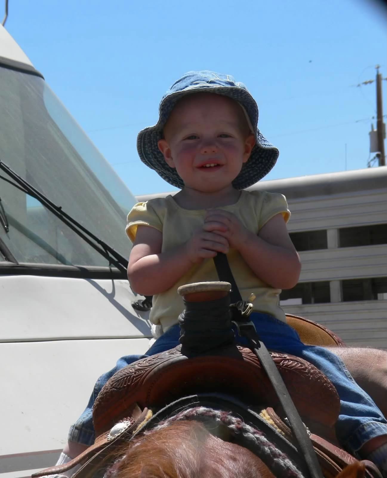 Olivia as a toddler in a denim bucket hat, smiling from a western saddle